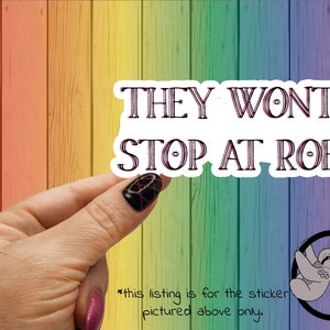 May include: White sticker with pink text that reads "THEY WONT STOP AT ROE". The sticker is being held by a hand with pink and black nail polish.