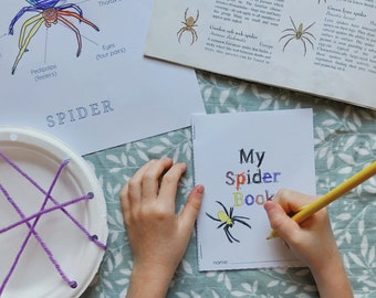 May include: A child's hand is drawing a yellow spider on a white paper with the words "My Spider Book" in colorful letters. The paper is on a green and white patterned surface.