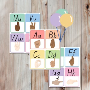 May include: Educational flashcards featuring the alphabet in American Sign Language (ASL). Each card displays a letter with a corresponding hand gesture, set against pastel backgrounds. Includes colorful balloons.