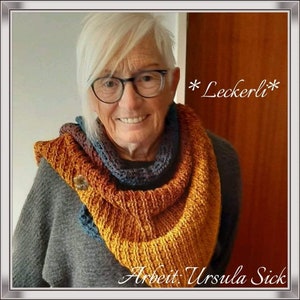 May include: A woman wearing a grey sweater and a multi-coloured crocheted scarf. The scarf is a mix of orange, brown, and blue. The text "*Leckerli*" is written in white on a brown background. The text "Arbeit: Ursula Sick" is written in white on a black background.