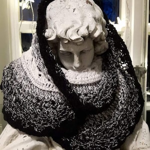 May include: A black and white ombre crochet cowl with a textured stitch pattern. The cowl is draped over a white plaster statue.