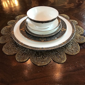 May include: A set of three white ceramic plates with gold and black trim, featuring a floral pattern. The plates are stacked on top of each other and are sitting on a gold beaded placemat.