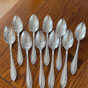 May include: A set of ten silver spoons with ornate handles. The spoons are arranged in a row on a wooden surface.