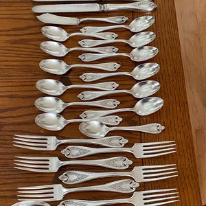 May include: A set of silverware, including forks, spoons, and knives, with ornate designs. The silverware is made of polished silver and has a vintage look.