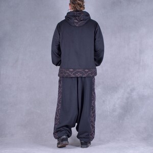 May include: Black hooded sweatshirt with a brown patterned trim around the bottom and hood. Black trousers with a brown patterned trim down the sides.