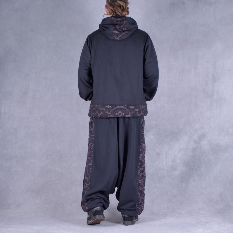 May include: Black hooded sweatshirt with a brown patterned trim around the bottom and hood. Black trousers with a brown patterned trim down the sides.