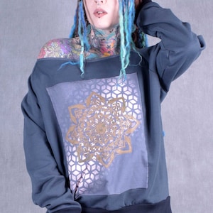 May include: A dark blue off-the-shoulder sweatshirt with a gold mandala design on the front. The sweatshirt has a relaxed fit and a ribbed hem.