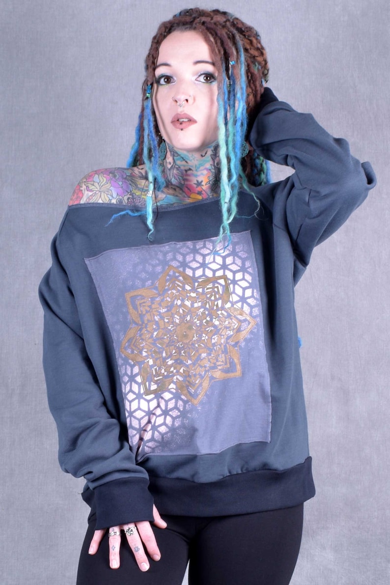 May include: A dark blue off-the-shoulder sweatshirt with a gold mandala design on the front. The sweatshirt has a relaxed fit and a ribbed hem.