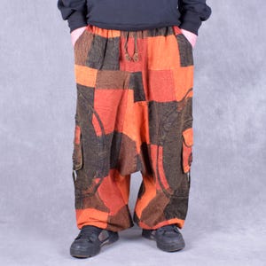 May include: Patchwork pants with a loose, baggy fit. The pants are made of a brown and orange fabric with a geometric pattern. The pants have a drawstring waistband and two large pockets on the sides.