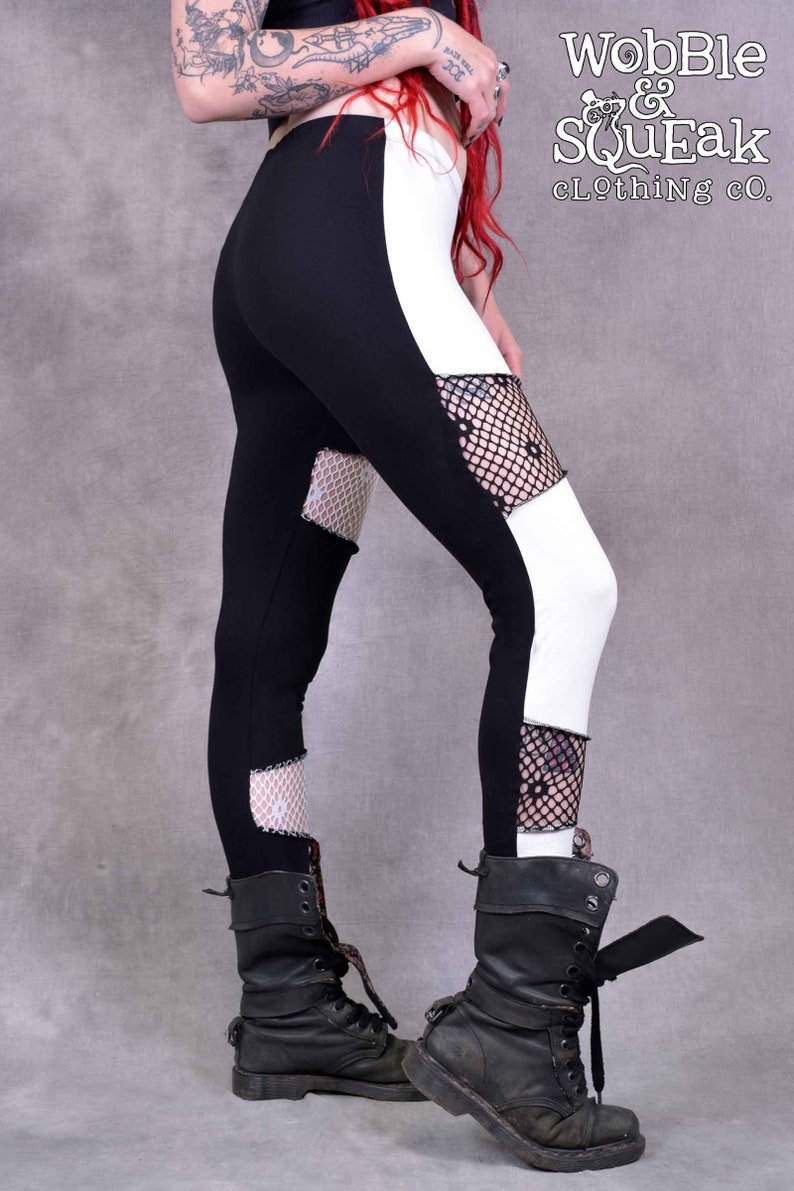 May include: Black and white leggings with fishnet panels. The leggings have a white panel on the right side and a black panel on the left side. The fishnet panels are on the lower legs. The leggings are worn with black boots.