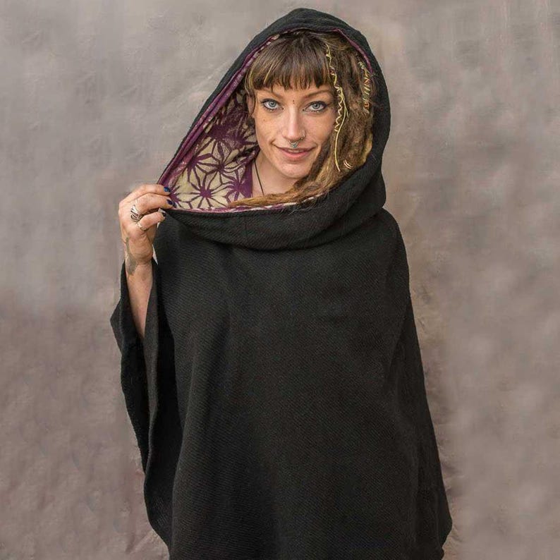 Puede incluir: Un poncho negro con capucha y forro floral morado y blanco. La capucha est&aacute; levantada y la persona que lleva el poncho tiene el pelo largo y casta&ntilde;o.