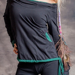 May include: Black long-sleeved shirt with a green trim and a green pocket. The shirt has a loose fit and a slightly off-the-shoulder neckline.