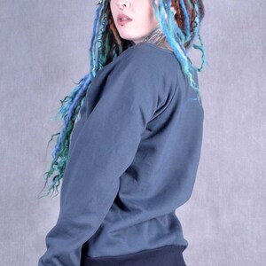 May include: A woman with blue and brown dreadlocks is wearing a dark blue sweatshirt with long sleeves and a black ribbed waistband. She is wearing black leggings and has a nose ring.
