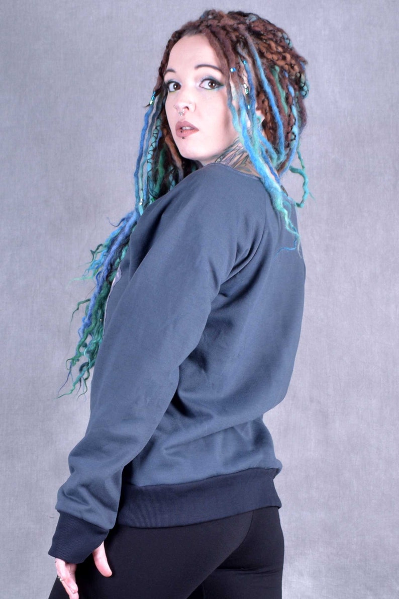 May include: A woman with blue and brown dreadlocks is wearing a dark blue sweatshirt with long sleeves and a black ribbed waistband. She is wearing black leggings and has a nose ring.