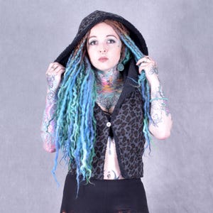 May include: A black and grey leopard print hooded vest. The vest has a single button fastening. The hood is black with a textured trim. The person in the image has blue and green dreadlocks and tattoos on their arms and neck.