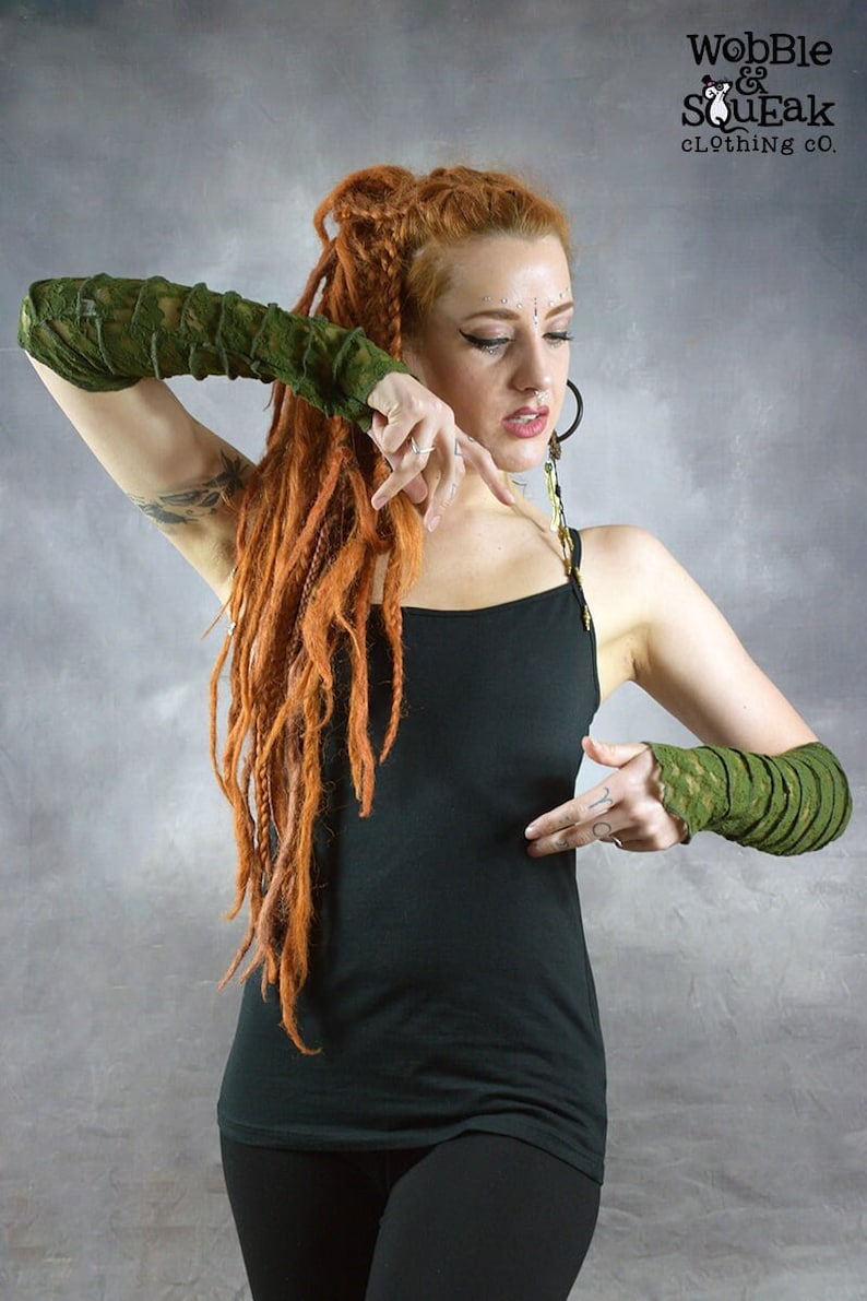May include: A woman with long red dreadlocks is wearing a black tank top and black pants. She is wearing green lace arm warmers on both arms. The arm warmers are made of a stretchy fabric and have a delicate lace design. The woman is posing with her arms raised, showing off the arm warmers.