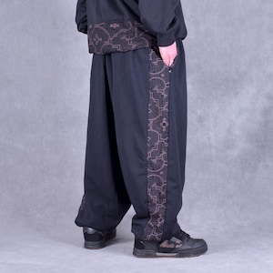 May include: Black sweatpants with a brown patterned stripe down the side. The sweatpants have a relaxed fit and a drawstring waistband.