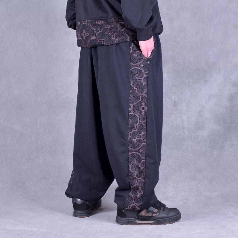 May include: Black sweatpants with a brown patterned stripe down the side. The sweatpants have a relaxed fit and a drawstring waistband.