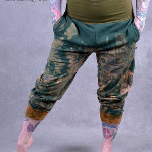 Op de afbeelding: Groene en bruine tie-dye broek met een brede groene tailleband. De broek is getailleerd bij de enkels en heeft een ontspannen pasvorm.