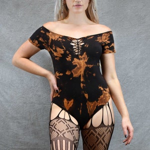 Peut inclure: Un body noir et brun tie-dye avec un détail de laçage à l'avant. Le body a des manches courtes et un décolleté arrondi. Le mannequin porte des bas résille noirs.