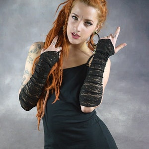 May include: A woman with long red dreadlocks is wearing a black tank top and black leggings. She is also wearing black lace fingerless gloves. The gloves are made of a delicate lace fabric and have a ruffled design. The woman is looking at the camera with a confident expression. The text "Wobble & SouEak Clothing Co." is visible in the top right corner of the image.