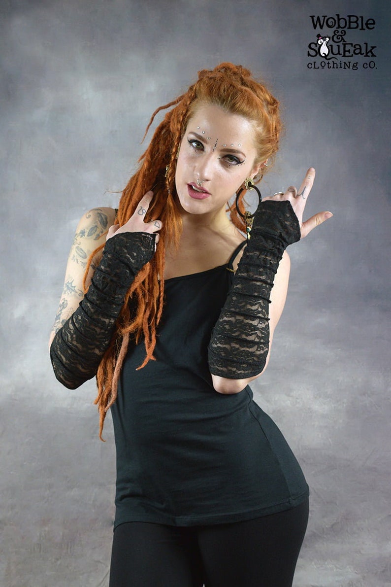 May include: A woman with long red dreadlocks is wearing a black tank top and black leggings. She is also wearing black lace fingerless gloves. The gloves are made of a delicate lace fabric and have a ruffled design. The woman is looking at the camera with a confident expression. The text "Wobble & SouEak Clothing Co." is visible in the top right corner of the image.