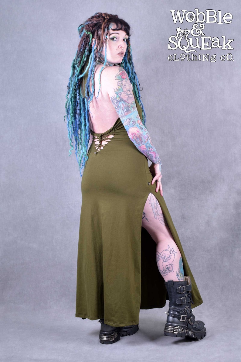 A woman wearing a long, olive green maxi dress with a lace-up back and a side slit. The dress is made of a soft, stretchy fabric and has a relaxed fit. The woman is wearing black boots with buckles.
