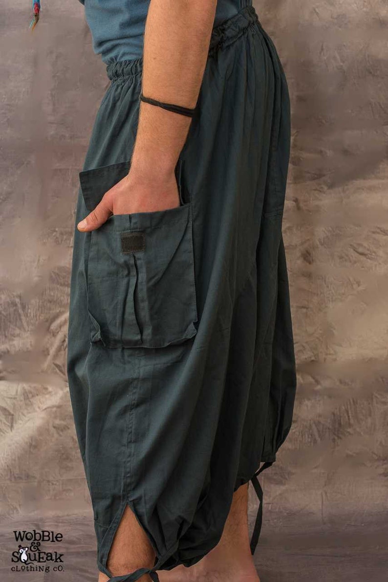 side view of Dark grey , loose-fitting trousers with a large cargo pocket on the left side. The trousers have a drawstring waistband and tie closures at the bottom of the legs.