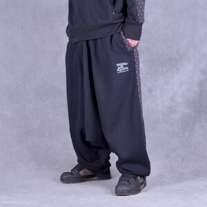 May include: Black sweatpants with a geometric pattern on the side. The sweatpants have a drawstring waistband and a logo that says "Wobble and Squeak Clothing Co."