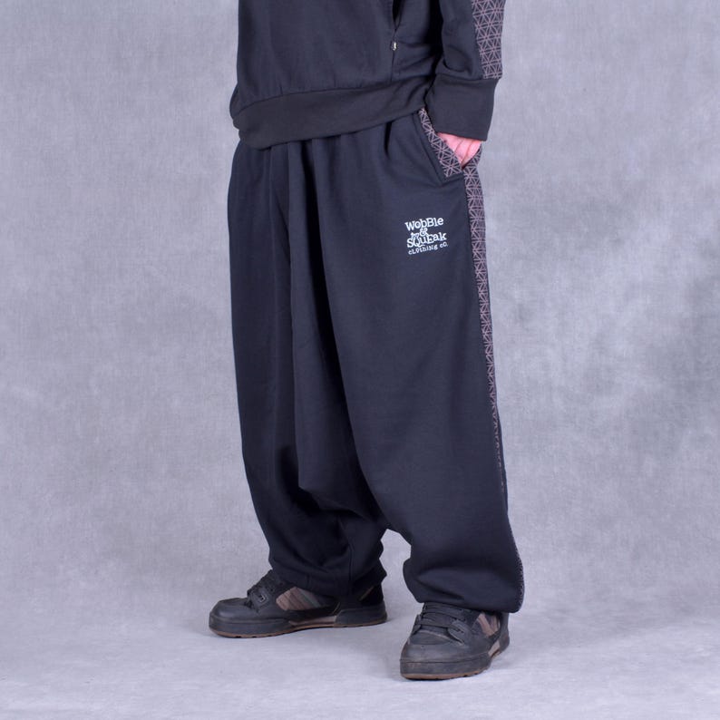 May include: Black sweatpants with a geometric pattern on the side. The sweatpants have a drawstring waistband and a logo that says "Wobble and Squeak Clothing Co."