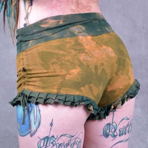 May include: Short shorts in a tie-dye style with a green and orange color scheme. The shorts have a ruffled hem and a gathered waistband. The shorts are made of a soft, comfortable material.