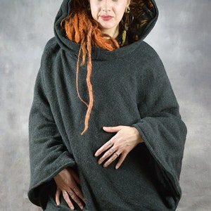 Puede incluir: Un poncho gris oscuro con capucha y forro estampado en negro y dorado. El poncho tiene mangas largas y un corte holgado.