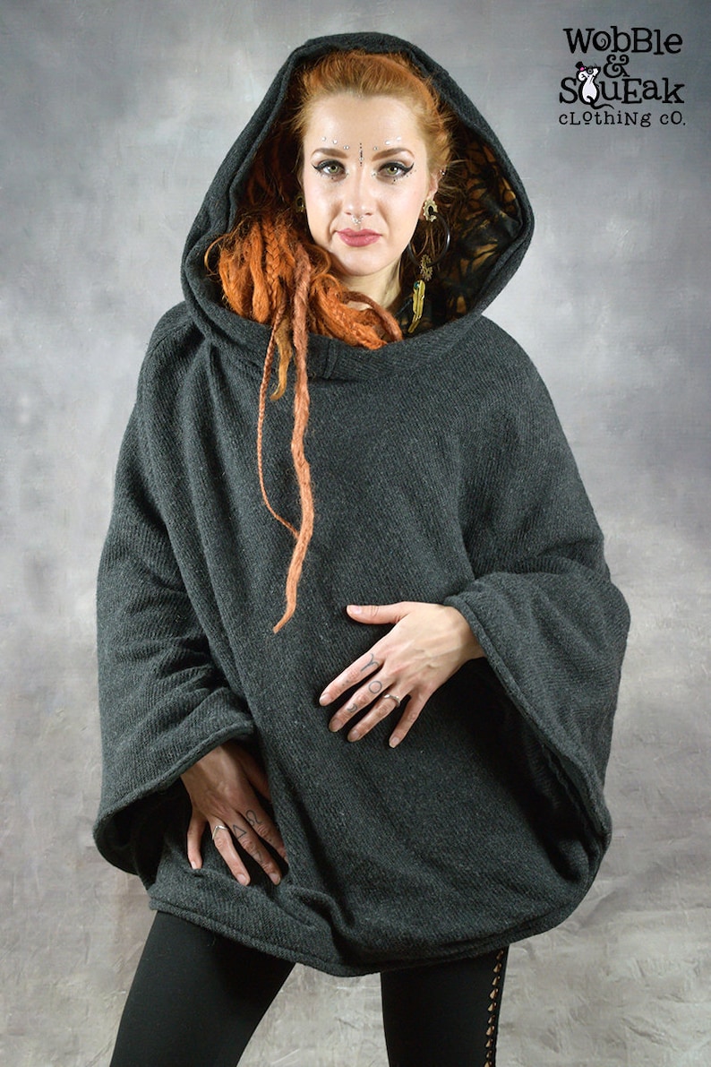 Puede incluir: Un poncho gris oscuro con capucha y forro estampado en negro y dorado. El poncho tiene mangas largas y un corte holgado.