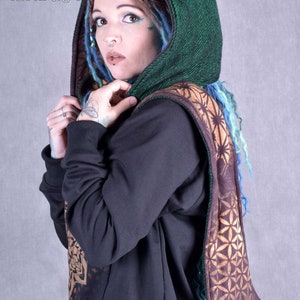 May include: A green hooded scarf with a brown and gold geometric pattern. The scarf is worn over a black sweatshirt.