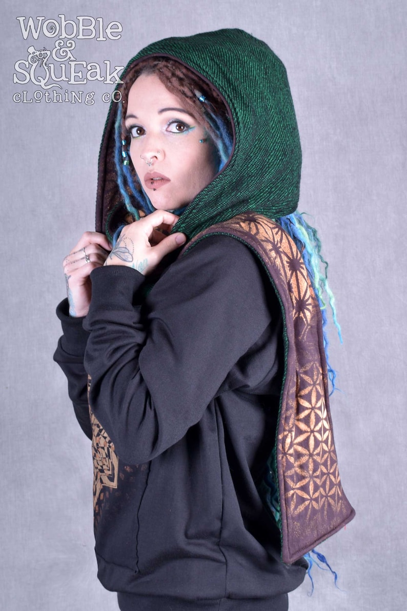 May include: A green hooded scarf with a brown and gold geometric pattern. The scarf is worn over a black sweatshirt.