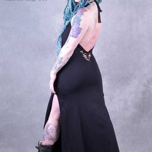 A black maxi dress with a lace-up back detail and a thigh-high slit. The dress is made from a soft, stretchy fabric and has a relaxed fit. The model is wearing the dress with black boots.