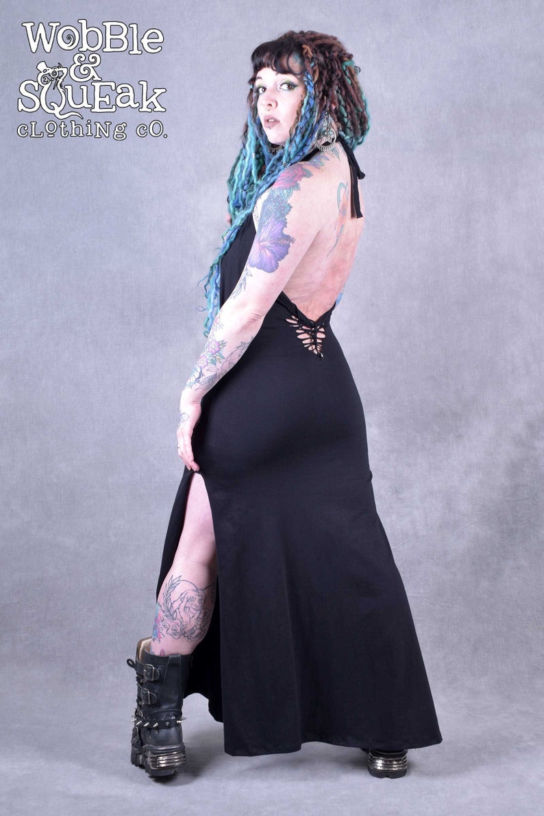 A black maxi dress with a lace-up back detail and a thigh-high slit. The dress is made from a soft, stretchy fabric and has a relaxed fit. The model is wearing the dress with black boots.