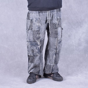 May include: Gray cargo pants with a distressed, patchwork design. The pants have multiple pockets and a drawstring waist.