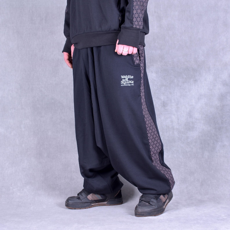 May include: Black trousers with a geometric pattern on the side. The trousers have a loose fit and a wide leg. The trousers have a logo on the side that says "Wobble & Slack Clothing Co."