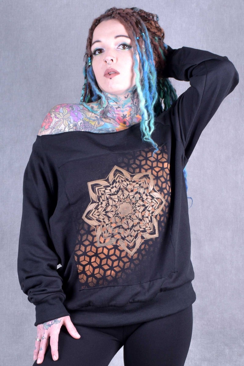 May include: Black off-the-shoulder sweatshirt with a gold geometric mandala design. The sweatshirt has long sleeves and a relaxed fit.