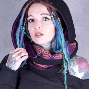 May include: A black hooded sweatshirt with a purple lining and a geometric pattern on the front. The hood is pulled up and the model is wearing a purple and orange scarf.