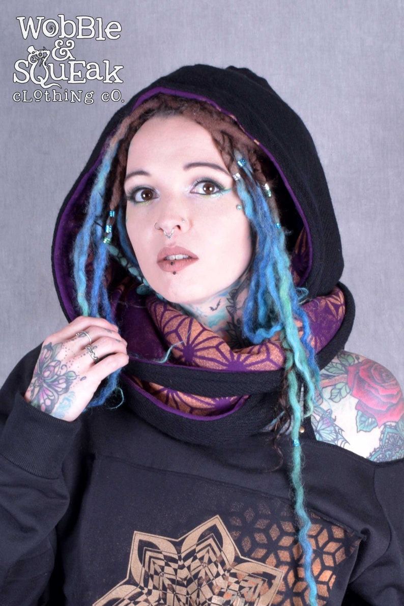 May include: A black hooded sweatshirt with a purple lining and a geometric pattern on the front. The hood is pulled up and the model is wearing a purple and orange scarf.