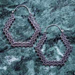 May include: A pair of silver-toned, geometric hoop earrings. The earrings have a hexagonal shape with intricate openwork detailing and small, decorative studs along the edges. The design features floral patterns.