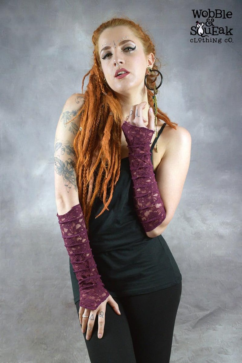 May include: A woman wearing a black tank top and black pants with a pair of long, burgundy lace fingerless gloves. The gloves are gathered at the wrist and have a delicate lace pattern. The woman has long, red dreadlocks and is wearing makeup. The image includes the text "Wobble & SouEak Clothing Co."