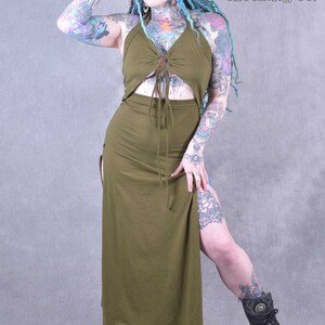 A long, army green maxi dress with a halter neckline and a tie at the waist. The dress has a side slit and a button detail at the chest. The model is wearing the dress with black boots.