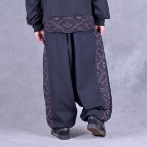 May include: Black trousers with a geometric pattern on the sides. The trousers are loose fitting and have a wide leg.