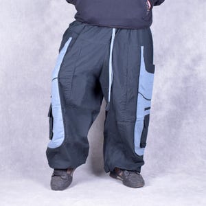 May include: Black and light blue cargo pants with a drawstring waist. The pants have light blue panels on the sides and pockets. The pants are made of a lightweight material and have a loose fit.