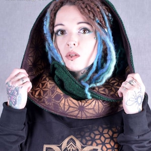 May include: A person wearing a black hooded sweatshirt with a gold geometric pattern. The hood is lined with a brown fabric with a gold geometric pattern. The person is wearing a green scarf with a brown border.
