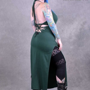 A dark green maxi dress with a lace-up back and a side slit. The dress is made from a soft, stretchy fabric and has a relaxed fit. The model is wearing the dress with black leggings and boots. it also has a knotted detail at the back