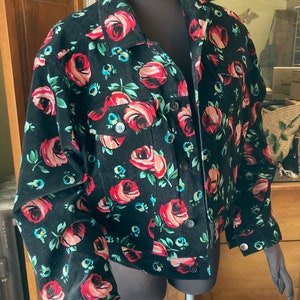 May include: A black corduroy jacket with a floral print of red roses and green leaves. The jacket has a button-up front and long sleeves.